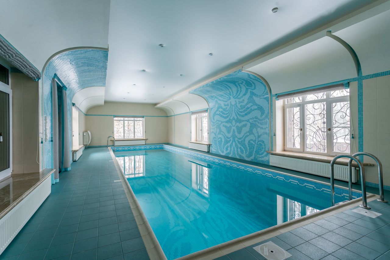 Spacious indoor swimming pool with beautiful blue tile design and natural lighting.