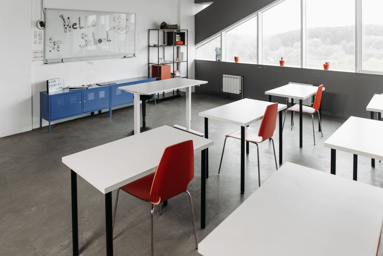 An empty classroom with red chairs, white tables, and natural light illuminating the space.